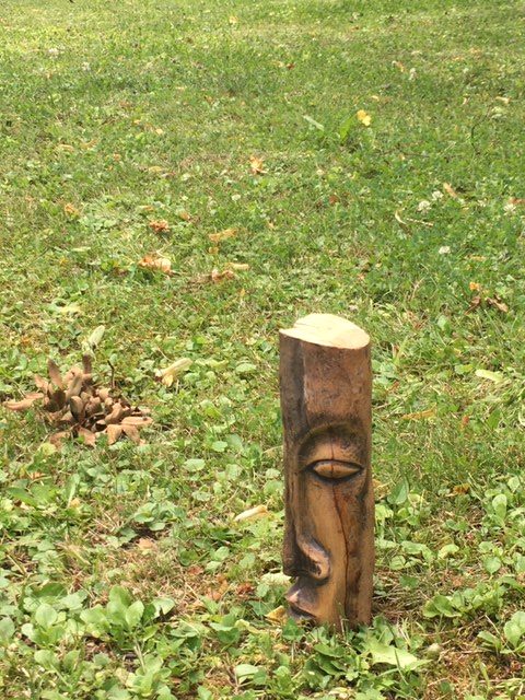 Holzstück in der Wiese, geschnitzte linke Gesichtshälfte