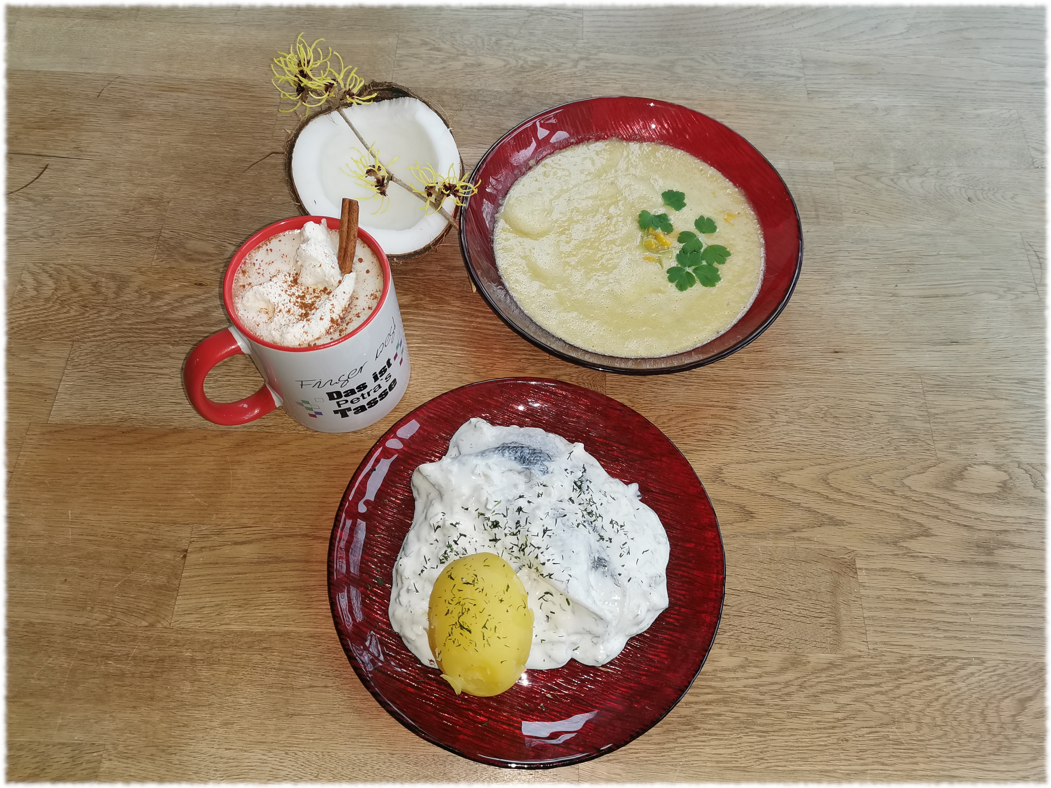 Matjessalat, Mais-Kokossuppe, heiße Schokolade - arrangiert auf einem Holztisch mit einer halben Kokosnuss und einem Zaubernuss-Zweig als Deko